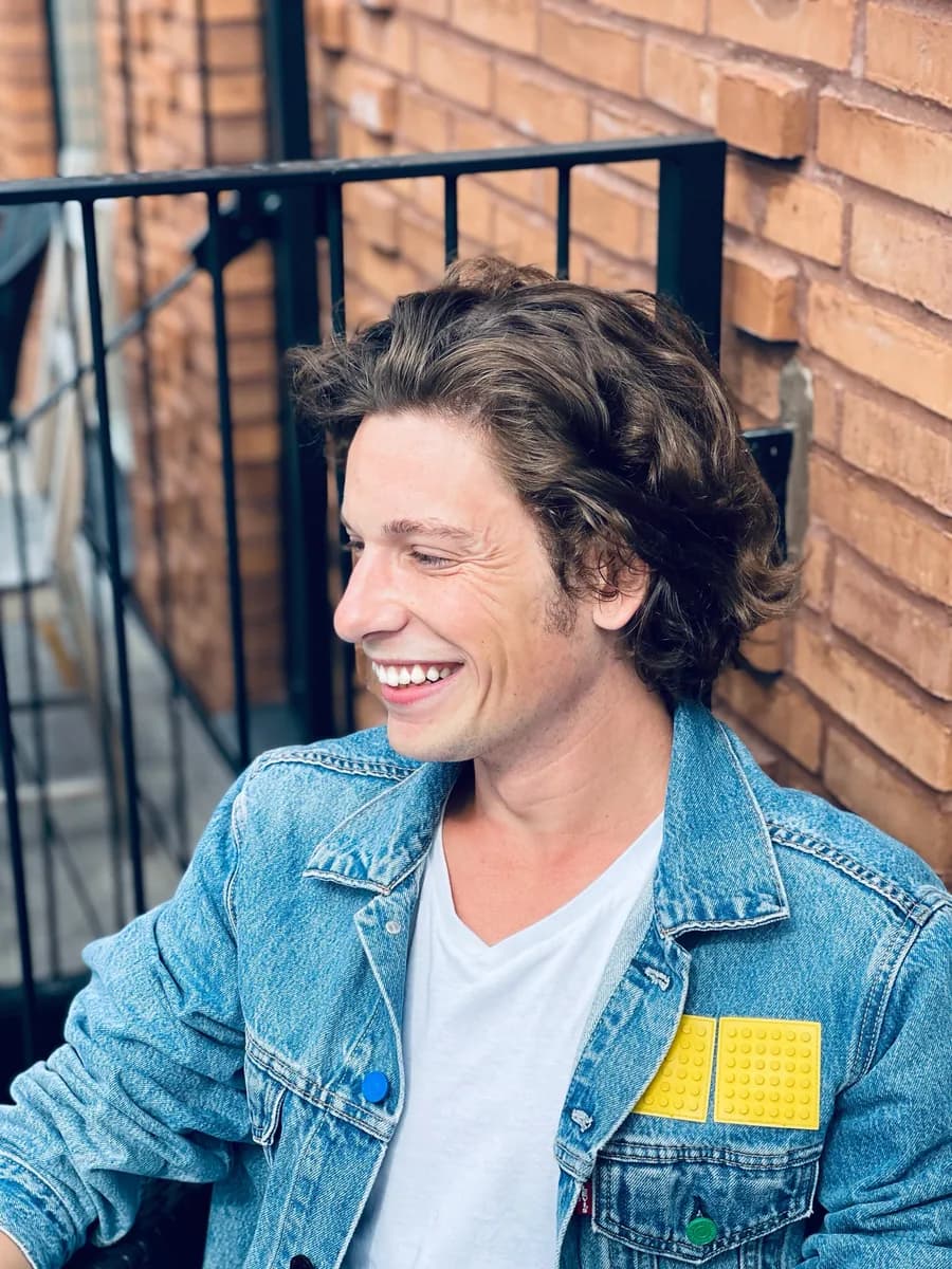 Mathieu, smiling, denim jacket in front of a brick wall